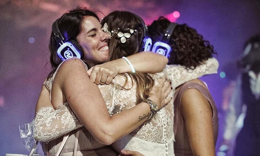 Matrimonio silentdisco Bride hugging friends while wearing silent disco headphones